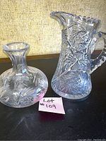 Photo showing both heavy cut glass water pitcher and bud vase together from front angle, highlighting intricate cut glass patterns and size comparison