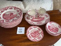 Photo showing the full set of Johnson Brothers "Old Britain Castles" china including dinner plates, cups on a platter, small plates, and salad plates with detailed red castle scenes