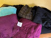Photo showing the variety of ladies winter capes and wraps including blue checkered, dark plaid, black, burgundy, purple, and plum colors.