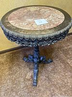 Full view of marble top round table with carved metal rim and tripod base