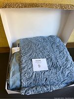 Blue fuzzy Dennis Basso throw in box, folded showing texture and color