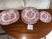 11 dinner plates, 1 salad plate, and 1 serving dish arranged on wood table showing pattern and lot tag
