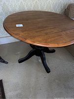 Solid wood round drop leaf table viewed from an angle showing tabletop and black pedestal base.