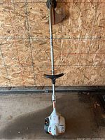 Full length image of the STIHL gas trimmer showing the white and orange plastic motor housing, metal shaft, and cutting guard.