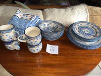 Photo of four stacked ceramic plates, bowls, four mugs, and folded matching kitchen towels on wood table with lot number card