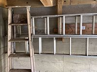 Photo showing wooden ladder and aluminum ladder 10 feet unexpanded leaning on wall in a garage or basement area.