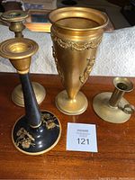 Photo showing three brass candlesticks and one brass vase, placed on wooden surface with lot number 121 card visible.