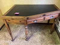 Left angled front view of a wooden corner desk with a black slate top, showing drawer and turned legs.