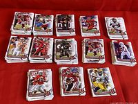 Multiple stacks of football cards arranged on a red surface, showing a variety of player images including quarterbacks, running backs, and wide receivers in different team uniforms.