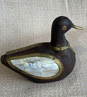 Front and side views of an antique wooden duck figurine featuring mother of pearl inlays on wings and chest with metal trim accents.