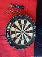 Front view of Nodor Supabull II dartboard with 6 darts above it on red cloth