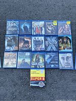 Top down photo showing all 16 DVD and Blu-ray movie cases arranged in rows on a dark textured surface.