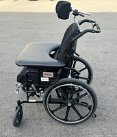 Side view of black Maple Leaf Supertils wheelchair showing padded seat and backrest, lap tray, large rear wheels, and caster wheels at front.