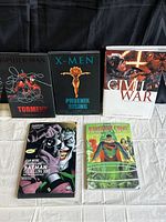 Five mixed Marvel and DC comic books shown standing upright on white cloth background