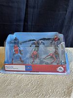 Six Marvel character figurines in original clear plastic packaging on a red base with Disney branding, showing Spider-Man, The Vulture, Iron Man, and others inside.