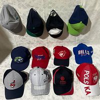 Set of 12 men's New Era baseball hats from various sports teams and brands laid out on a white surface.