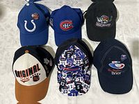 Set of six men's sports caps including NHL teams and other sports logos arranged in two rows on a light surface.