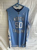 Front full view of blue North Carolina jersey with number 50 and Jordan logo, showing argyle side panels and neckline, hung on blue plastic hanger.