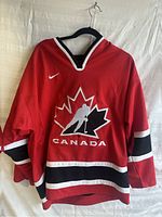 Front view of the red Nike Team Canada hockey jersey showing the large maple leaf logo with hockey player silhouette and Nike swoosh on the upper chest.