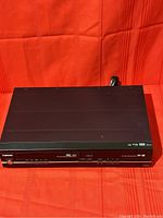 Front view of Toshiba DVD Recorder and VCR combo on red surface, showing buttons and indicators