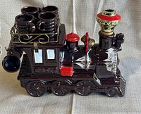 Front-side view of brown ceramic train-shaped whiskey decanter with six small ceramic cups attached in metal holder on top.