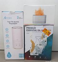 Front view of packaging for Acare Top Fill Aroma Humidifier, Premium Essential Oil Diffuser, and another small device showing condition and branding