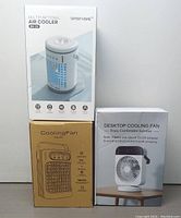 Photo of three boxed portable air cooling devices: multifunctional air cooler, desktop fan, and compact cooling fan boxes stacked.
