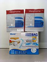 Two boxes of Meiqihome 8-pack vacuum storage bags and one box of Warmi 16-pack vacuum storage bags with pump and clips shown together.