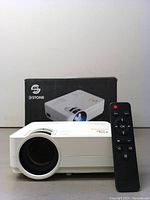 White 3Stone projector and black remote control placed in front of the product box showing an image of the same projector.