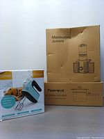Three original boxes arranged side by side: large box for masticating juicers, box for Topwit Electric Hot Pot, and box for Yomelo 9-speed Hand Mixer.
