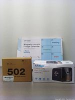 Photo showing boxed items in the lot including the SWSKR Magnetic Acrylic Fridge Calendar 2 pack, 502 printer ink refill bottles box, and AFMAT Heavy Duty Pencil Sharpener box