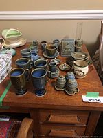 Full view of assorted Irish porcelain items arranged on wood table: mugs, cups, plates, teapot, pitcher, oil lamp.