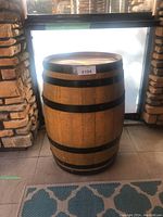 Full frontal view of wooden barrel with black metal bands sitting indoors on a tile floor.