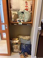 Shelf displaying a variety of decorative pillows and two ceramic mugs, showing overall lot contents.