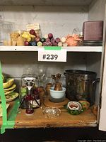 Wide photo of two shelves containing assorted candles, wine glasses, wine openers, wooden kitchen tools, and decorative bowls.