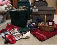 Two large Rubbermaid storage bins filled with Christmas-themed fabrics and additional linens and holiday decorations arranged in front of them.