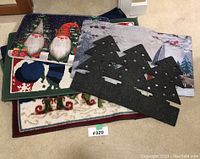 Photo showing a set of five Christmas-themed floor mats and a black tree-shaped decorative cutout laid on carpeted floor.