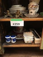 Two shelves inside hutch with Christmas servingware including snowman salt and pepper shakers, square serving dishes with Christmas trees, holiday-themed plates, and a ceramic fondue pot with reindeer design.