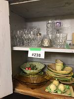 Shelf with crystal stemware including wine and sherry glasses, clear cut glass vase, antique leaf-pattern ceramic dishes and condiment holders.