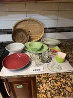 Lot displayed on granite kitchen counter, showing all ceramic dishes, glass espresso cups with saucers, colorful small dishes, and woven trays.