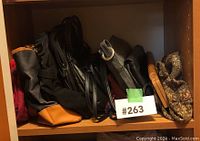 Shelf with six assorted bags and purses in various materials including leather and fabric.