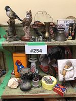 Front view of assorted figurines, thimbles, and small decorative items arranged on two shelves including bird figurines, tins, metal thimbles, small brass vase, and angel figurine.