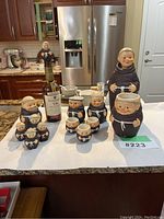 Overall view of the 12-piece Friar Tuck ceramic collection arranged around a bottle for scale, showing the diversity of item sizes and forms.