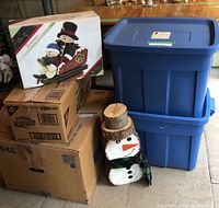 Photo of stacked cardboard boxes and 2 Rubbermaid bins with a wooden snowman figure in front