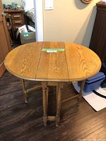 Round oak folding accent table with folded-out legs on wood floor near doorway.