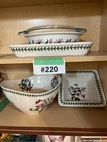 Shelf shot showing all items: Pyrex round glass dish with lid inside rectangular PortMeirion Botanical ceramic dish on top shelf; large botanical bowl and small square dish on lower shelf.