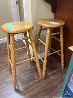 Photo showing the pair of wooden bar stools with visible round seats, spindle legs, and horizontal footrest bars.