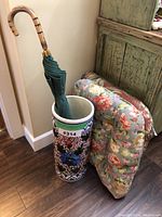 Photo of Spanish-style ceramic umbrella stand with umbrella and blue floral seat cushions leaning against a green hutch.