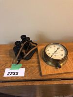 Full view of vintage binoculars with leather strap and pressure gauge on wooden base next to each other