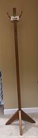 Full view of the tall wooden coat rack with tri-legged base and metal hooks for hanging coats.